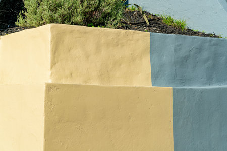 Double retaining wall on side of property with visible plants and shade and sun on exterior. Beige or cream colored paint with stucco texture and flat angular design.の写真素材