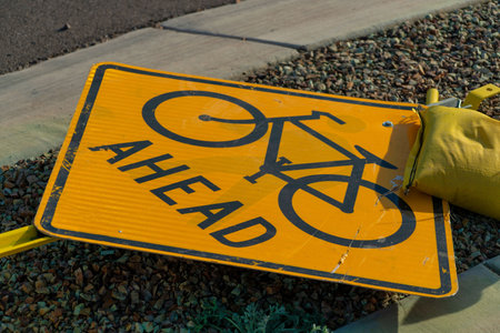 Road sign taken down by a storm or damage with sand bags on the sign with black paint and yellow color exterior. In an urban area or in the neighborhood on the side walk near gravel.の写真素材