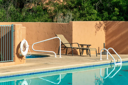Pool side view with orange stucco wall and metal hand rails with water and cement with saftey float in midday sun. Pool in apartment complex or community public area used for swimming and recreation.の写真素材