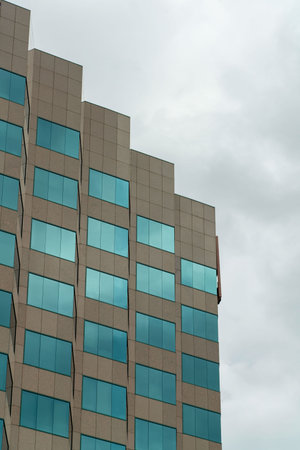 Building for business with rigid geometric design or shape with blue windows and zig zag angles with gray sky background. Blue visible windows in silicon valley and modern downtown urban area of town.の写真素材