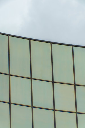 Modern office building facade with sleek glass pannels and gray skies in the late afternoon shade in...