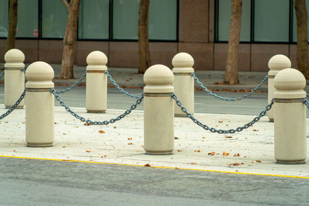 Gaurd rails in road or in courtyard with metal chains and cement posts in late afternoon sun in urban area and road. In the city in urban or industrial area of town with building background.の写真素材