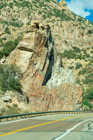 Bright sun beaten road with yellow and white lines and asphalt with metal hand rails and sunny rock face cliffs. Cloudy blue sky in daily sunlight in arizona in the desert mountains.の写真素材