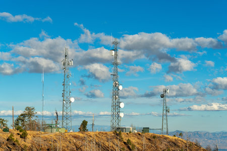 Row of industrial radio towers on summit of mountain in arizona with cloudy desert skies and blue with dry grass. Hills in industrial area for internet connection and radio and cell phone connection.の写真素材