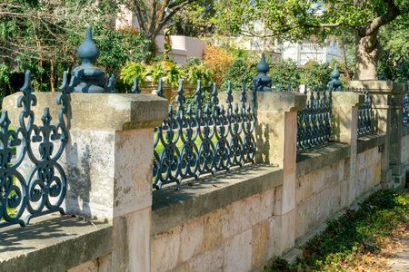 Brick and cement retaning wall with metal decorative gates and fancy lanterns with trees and plants in midday sun. Late afternoon in suburban neighborhood or front yard fence and rusty posts.の写真素材