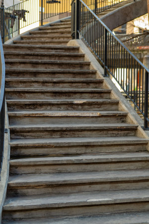 Row of stairs that tapper toward top of tamp with black metal hand rail in late afternoon shade in...