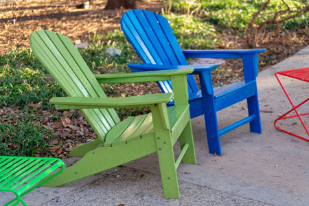 Colorful chairs on deck or patio in the back or front yard with green and blue seats on cement sidewalk in neighborhood home. House in city with urban or suburban barbeque lounge with green grass.の写真素材