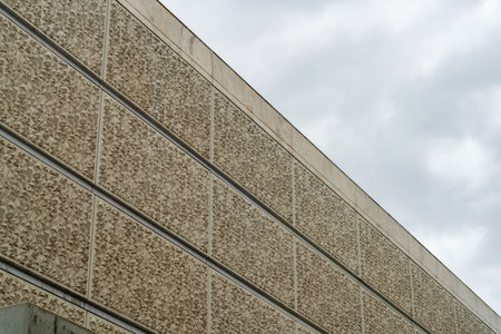 Ridged and textured building or wall facade with geometric block and rectangle design with flat roof and background clouds. Late afternoon shade in city or in industrial area of commercial districts.の写真素材