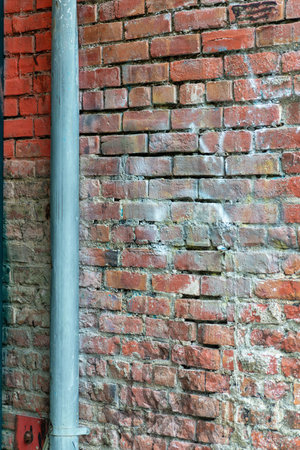 Metal pole with with aged and weathered brick wall in afternoon shade in downtown city urban area...