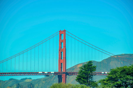 Golden gate bridge in suburban distance with natural hills and ocean mountain background in san francisco california. Historic districts with red color suspension pathway across ocean with trees.の写真素材