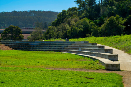 Open park or auditorium area with grass and natural background trees on mountains and blue sky in afternoon sun. In suburban outdoor area for walking dogs and recreating downtown.の写真素材