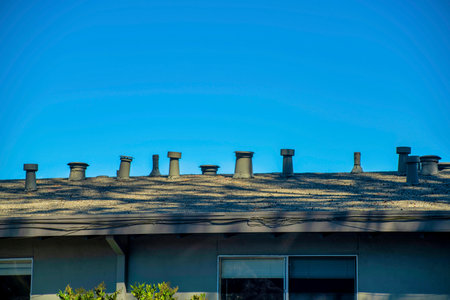 House or home rooftop with a great many chimney vents metal on top of building with clear blue skies above. In downtown neighborhood in city for fireplace and late eveing sunlight shade.の写真素材