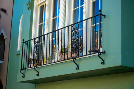 Black metal decorative small balcony with flowers and white arched window frames on exterior of house or home. Downtown neighborhood with green stucco facade in modern suburb.の写真素材