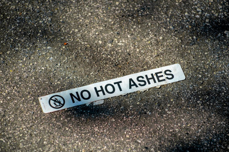 Sign that says no hot ashes on floor of barbeque location with white and black paint in late afternoon shadow. Asphalt floor in park or outdoor area for camping and recreation.の写真素材