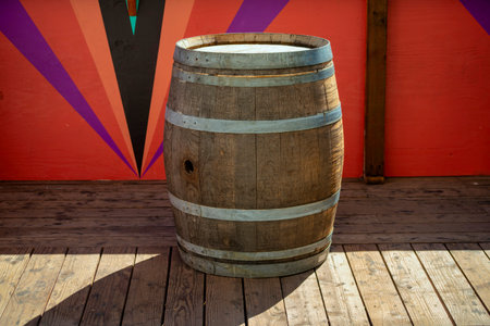 Wooden barrel sitting on panneled floor at carnival or on a ship for transporting foods and liquids with metal rings. Background red wall in city or in rural area for whiskey and other products drum.の写真素材