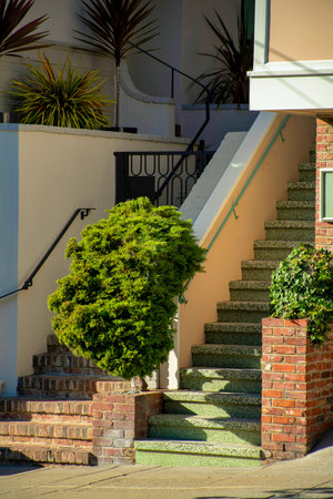 Front porch entranceway with brown brick facade and beige stucco cement with shrubs and sidewalk on...