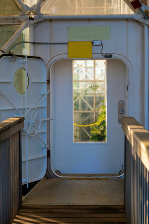 Bulkhead or lockable metal door and gate inside of greenhouse in scientific research facility with wooden bridge. In afternoon shade indoors with green trees and plants in background.の写真素材