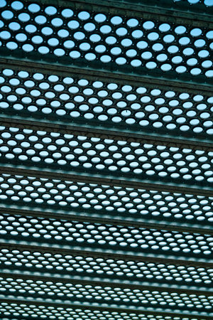 Black metal grate or drain vent with holes in geometric pattern for background or texture image with background sky. In industrial area with light pattern and horizonal beams in city.の写真素材