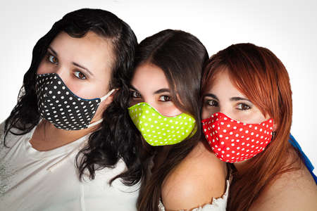 three female friends with colorful face mask protect themselves from covid coronavirus 19 isolated on white backgroundの写真素材