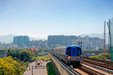 Scenic view of a metro train traveling on elevated rails of public metro System and residential buildings crowding in background under blue clear sky in Zhongli, Taoyuan City, Taiwan, Asiaのeditorial素材
