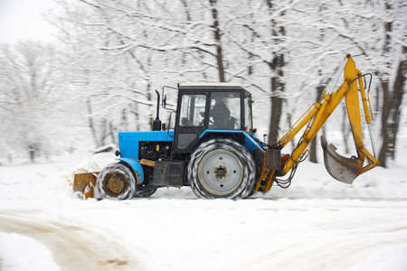 The tractor of dark blue color deletes snow in park