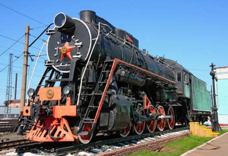 Old black locomotive in the railway depot in the parking lot.