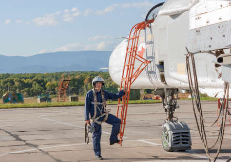 Military pilot in helmet stands near jet plane.