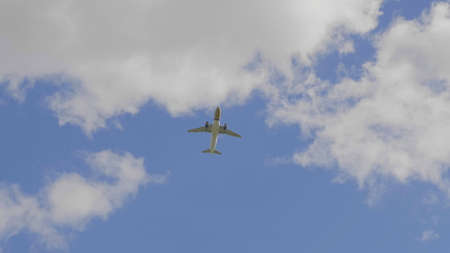 Commercial passenger airplane flying overhead on sunny day.