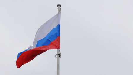 Russian flag on the flagpole waving in the wind against a blue sky with clouds.の写真素材