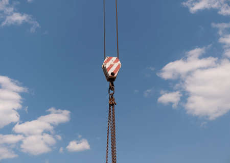 Crane hook with red and white stripes hanging, blue sky in background.の写真素材