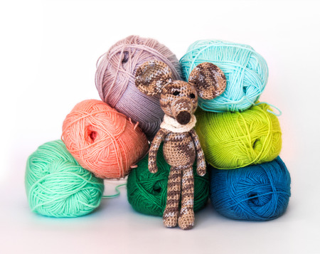 small colorful knitted toy mouse in a white scarf playing with colored yarn, threads of wool, Bright children's toy, clew, knitted mouse between skeinsの写真素材