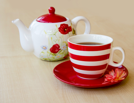 Striped cup with tea on a saucer and brewer with a poppy picture on a wooden table top and red rose flowerの写真素材