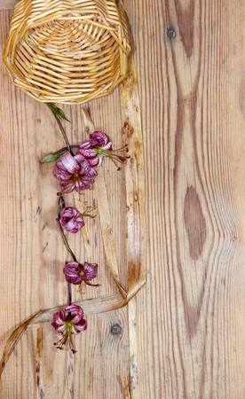 Dried wilted lilies scattered from fallen wicker basket on a  dark wooden surfaceの写真素材