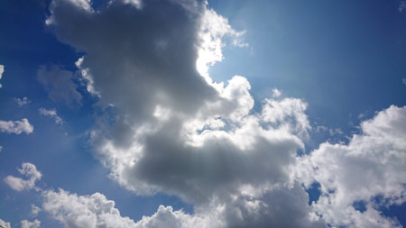Bright sun rays pierce cumulus clouds in a vivid blue sky, creating dramatic light and shadow...