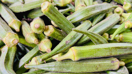 A detailed close-up view of a pile of fresh, raw green okra pods. Perfect for healthy eating,...