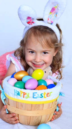 Toddler girl with bunny ears  holding a basket full with Easter colorful eggsの写真素材
