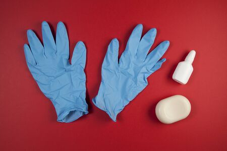 Latex or rubber gloves, a bar of soap and antiseptic gel on a red background. Close-up, top view, place for text.の写真素材
