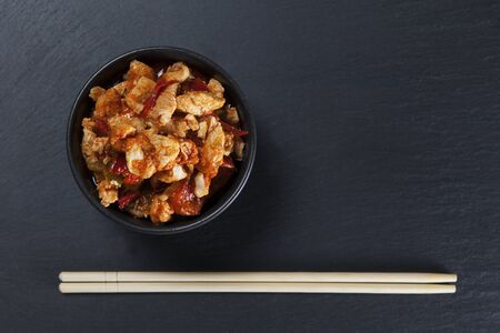 Kung Pao Chicken or Gong Bao Ji Ding at dark slate background. Sichuan Kung Pao is chinese cuisine dish with chicken meat, chilli peppers, sauces and onion. Copy space. Top view.の写真素材