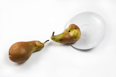Funny concept - reduction of food waste. Ugly vegetables and fruits. Two ugly pears are trying to get on the plate. Isolated image on a white background.の写真素材