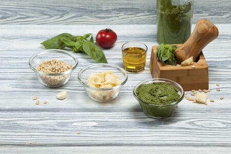 Traditional italian basil pesto sauce and its ingredients on a light wooden background. Closeup. Selective focus.の写真素材