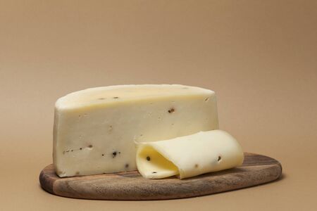 Italian Caciotta cheese with black peppercorns. Half of the cheese head lies on a wooden board. Closeup. Place for text.の写真素材