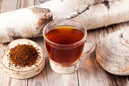 Chaga tea - a strong antioxidant, boosts immune system, has detox quality, improves digestive. A mug of healing drink is on the table next to a birch mushroom.の写真素材