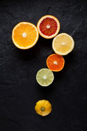 Halves of fresh ripe citrus are laid out in the form of a question mark on a dark stone background. Top view.の写真素材