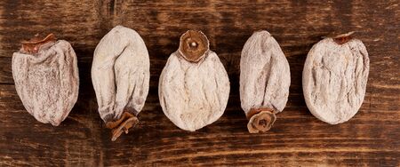 Five flattened dried persimmon fruits on a brown wooden board. Top view.の写真素材