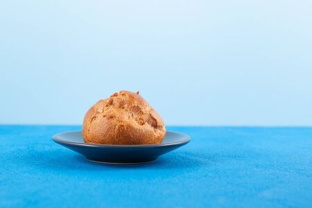 Fresh golden crispy bun on a plate, close-up. Light blue background, copy space.
