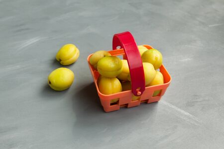 Yellow-green apricots in a shopping basket. Latest trend - Eating unripe fruits.  Gray background,...