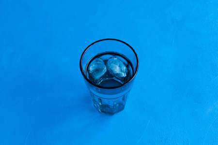 Pure drinking water with ice in a transparent blue glass on a blue background. Top view, selective...