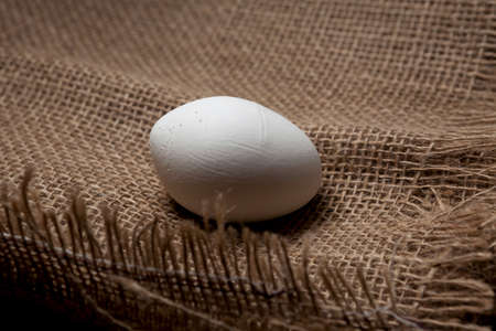 Ugly abnormal crooked egg on the background of burlap, close-up.の写真素材