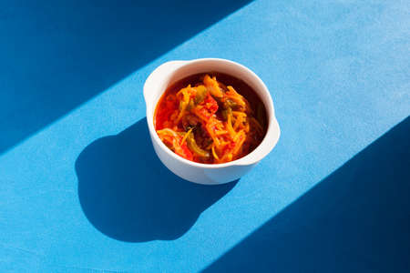 Delicious juicy stewed vegetables in a spicy tomato sauce in a white bowl, top view. Sunlight and...