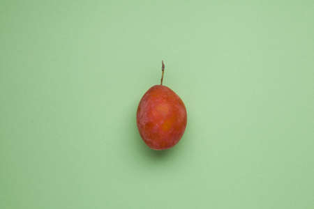 Unripe plum or prune on a green background. Flat lay, top view, copy space.